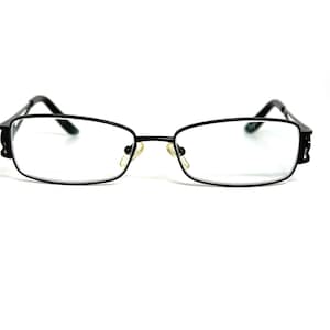 May include: A pair of black rectangular eyeglasses with thin frames and clear lenses. The glasses feature adjustable gold-toned nose pads and black temples that extend from the outer corners of the frame, providing a simple and functional design.