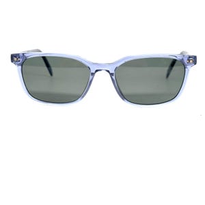 May include: Light blue sunglasses with a rectangular frame and dark lenses. The sunglasses have a classic design with a subtle, translucent frame. The temples are dark, and the lenses are a dark gray color.