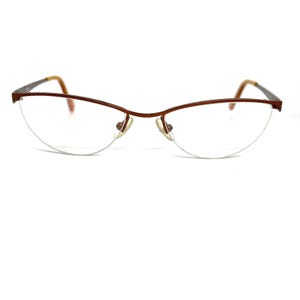 May include: Brown metal-framed eyeglasses with a half-rim design. The lenses are clear, and the frame has a thin, delicate appearance. The temples are a lighter brown color. The glasses have a classic, understated style.