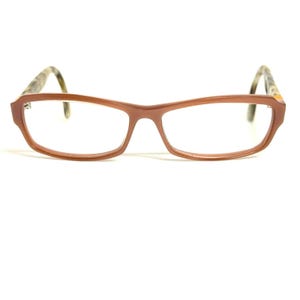 May include: Rectangular eyeglasses featuring a solid terracotta-colored frame with a smooth finish. The temples are patterned with a mottled brown and beige tortoiseshell design, extending from the front frame to the curved ear pieces.