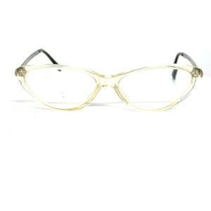 May include: Clear cat-eye eyeglasses with a light yellow frame and dark gray temples. The lenses are clear, and the frame has a subtle, vintage aesthetic. The glasses are designed for vision correction.