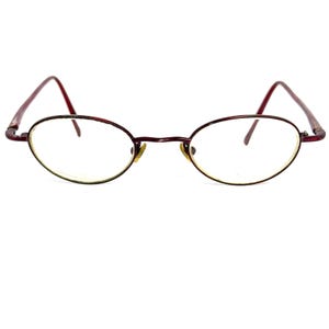 Peut inclure: Une paire de lunettes de vue ovales avec une monture en métal bordeaux et des verres transparents.