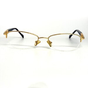 Peut inclure: Lunettes à monture dorée avec un design demi-monture. Les lunettes présentent une monture dorée délicate, des branches noires et des verres transparents. Le pont et les branches ont des accents décoratifs. Le style général est vintage et élégant.