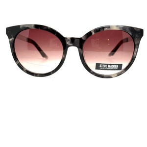 May include: Round sunglasses with a marbled grey and black pattern. The lenses have a brown gradient, darker at the top and fading to a lighter shade at the bottom. The brand name "STEVE MADDEN" is printed on the right lens.
