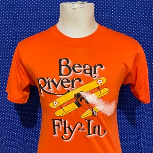 May include: Orange t-shirt with a graphic of a yellow airplane and the text "Bear River Fly-In".