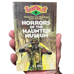 May include: A paperback book cover with a yellow, green, and red title "Twistaplot" with the number 9 in a circle. The book title is "Horrors of the Haunted Museum" with an illustration of a mummy in a hallway.