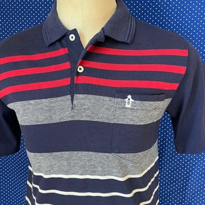 May include: A striped navy blue polo shirt with red and white stripes. The shirt has a pocket on the left side.