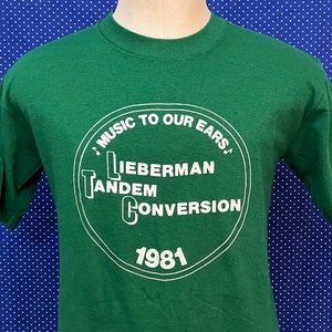 Puede incluir: Camiseta verde con un gráfico circular blanco que dice "Music to our ears" y "Lieberman Tandem Conversion 1981".