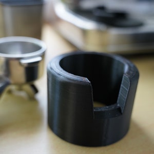 Könnte beinhalten: Ein schwarzer 3D-gedruckter Kaffeettamperhalter mit einem Ausschnitt für einen Siebträger.