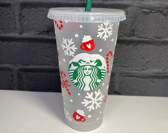 May include: A clear, reusable cold beverage cup with a green straw. The cup features a holiday design with snowflakes, candy canes, and red coffee cup graphics. The Starbucks logo is prominently displayed in the center.