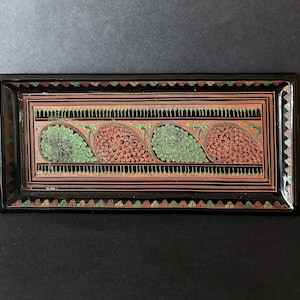 May include: A rectangular black tray featuring a central horizontal band decorated with alternating green and reddish-brown paisley-shaped floral motifs. The border is accented with thin lines and small repeating leaf patterns in green and gold.