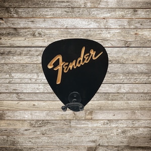 May include: Black wooden guitar pick shaped wall hook with the word "Fender" in gold lettering.