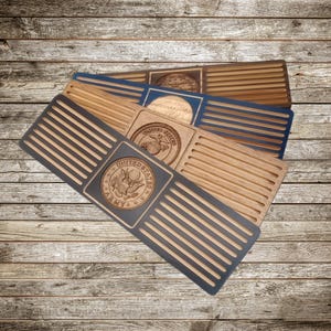 May include: Wooden coasters with a slotted design and engraved military emblems. The coasters are in various colors, including natural wood, blue, and gray. Each coaster features a different emblem, such as the United States Army seal.