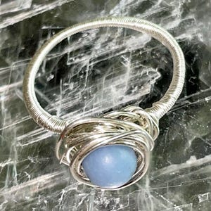 Può includere: Un anello avvolto in filo d'argento con una pietra preziosa blu chiaro.