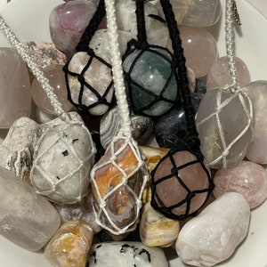 Puede incluir: Un bol lleno de varias piedras lisas y pulidas, algunas de las cuales están envueltas en hilo de macramé blanco y negro. Las piedras son en tonos de blanco, gris, rosa, verde y marrón.