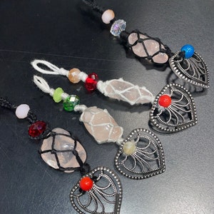 Puede incluir: Cuatro amuletos de cristal rosa con cuerda negra y colgantes de corazón plateados. Cada amuleto tiene una cuenta de color diferente y un estilo de anudado diferente.