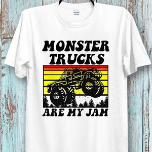 May include: White t-shirt with a black and white graphic of a monster truck with the text "Monster Trucks Are My Jam" in black and yellow.