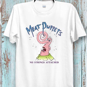 May include: White t-shirt with a graphic of a cartoon character with a long nose and the text "Meat Puppets No Strings Attached".