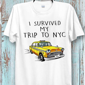 May include: White t-shirt with black text that reads "I survived my trip to NYC" and a yellow taxi cab illustration.