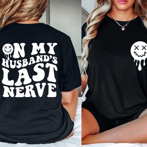 K&ouml;nnte beinhalten: Schwarzes T-Shirt mit wei&szlig;em Text, der "On My Husband's Last Nerve" lautet, und einem tropfenden Smiley mit X f&uuml;r Augen.