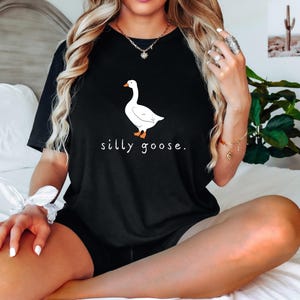 K&ouml;nnte beinhalten: Ein schwarzes T-Shirt mit einem wei&szlig;en G&auml;nse-Motiv und dem Text "silly goose."