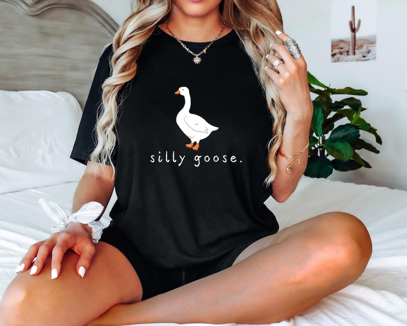 K&ouml;nnte beinhalten: Ein schwarzes T-Shirt mit einem wei&szlig;en G&auml;nse-Motiv und dem Text "silly goose."