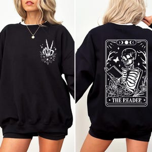 May include: Black sweatshirt with a white skeleton hand making a peace sign on the front and a tarot card design on the back that says "The Reader".