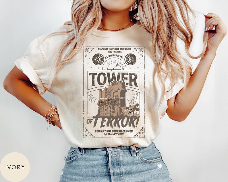 May include: Ivory-colored t-shirt featuring a vintage-style graphic for the Tower of Terror ride. The design includes the ride's name, a spooky building illustration, and the text "You may not come back from The Twilight Zone."