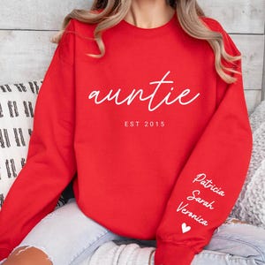 May include: Red sweatshirt with the text "auntie est 2015" on the front and the names "Patricia, Sarah, Veronica" and a heart on the left sleeve.