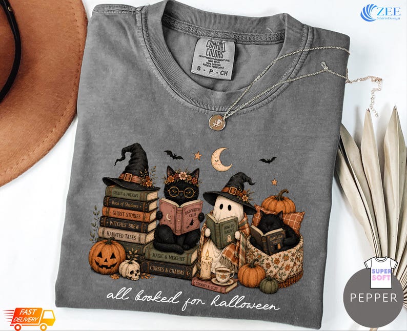 A gray t-shirt with a Halloween-themed graphic design featuring cats dressed as witches and wizards, along with various Halloween-related items such as pumpkins, bats, and a crescent moon.