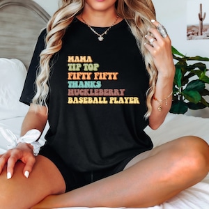 May include: Black t-shirt with retro-style text in various colors. The text includes words like "Mama," "Tip Top," and "Baseball Player." The shirt has a relaxed fit and is suitable for casual wear.