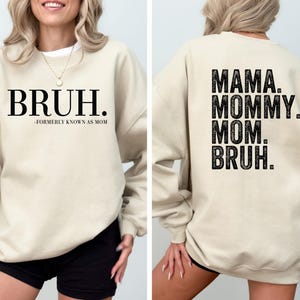 May include: A beige sweatshirt with black text. The front of the sweatshirt says "BRUH. -FORMERLY KNOWN AS MOM". The back of the sweatshirt says "MAMA. MOMMY. MOM. BRUH."