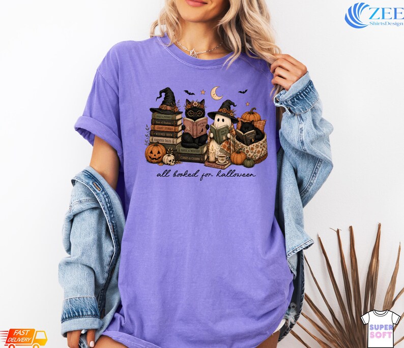 A woman wearing a purple t-shirt with a Halloween-themed graphic of cats and a book, along with the text "all baked for halloween".