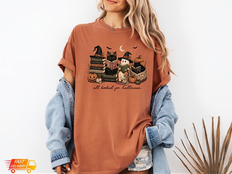 A woman wearing a t-shirt with a Halloween-themed graphic design, including books, pumpkins, bats, and a cat.