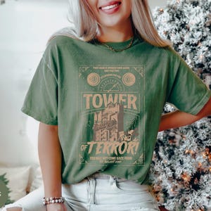 May include: Moss green t-shirt with a graphic featuring the words "Tower of Terror" and the text "That God is speaking once again and the time is speaking for you". The shirt has a vintage, distressed look.
