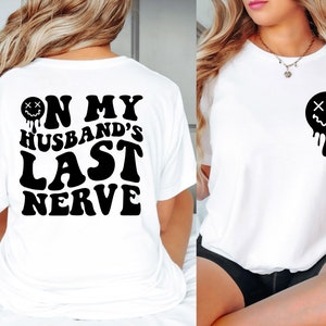 K&ouml;nnte beinhalten: Zwei wei&szlig;e T-Shirts mit schwarzem Text und einer schwarzen Grafik. Die Vorderseite eines Shirts hat ein tropfendes Smiley-Gesicht mit X f&uuml;r Augen. Die R&uuml;ckseite des anderen Shirts sagt "On My Husband's Last Nerve" mit einem tropfenden Smiley-Gesicht mit X f&uuml;r Augen.