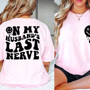K&ouml;nnte beinhalten: Pinkes T-Shirt mit schwarzem Text, der "On My Husband's Last Nerve" lautet, und einem tropfenden schwarzen Smiley mit X f&uuml;r Augen.