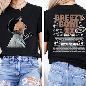 May include: Black t-shirt featuring a portrait of a man wearing a baseball cap and a denim jacket. The front of the shirt has a signature. The back of the shirt has the text "Breezy Bowl XX Stadium World Tour" with a list of tour dates.