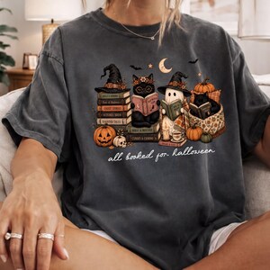 A person wearing a t-shirt with a Halloween-themed graphic design, including a witch, a cat, and various Halloween-related elements.