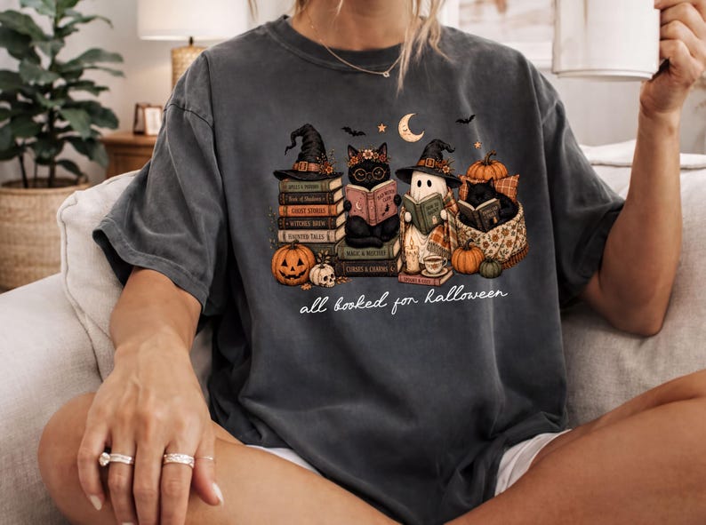 A person wearing a t-shirt with a Halloween-themed graphic design, including a witch, a cat, and various Halloween-related elements.
