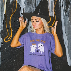May include: A purple t-shirt with a graphic of two ghosts holding hands with a spider between them. The text "OPAL AND JUNE" is above the ghosts and "your spooky design here" is below. The model is wearing a black witch hat and fishnet tights.