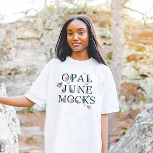 K&ouml;nnte beinhalten: Wei&szlig;es Oversize-T-Shirt mit floralem Design und dem Aufdruck "OPAL and JUNE MOCKS" auf der Vorderseite.