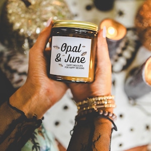 Può includere: Un barattolo di vetro marrone per candele con un coperchio dorato. L'etichetta sul barattolo recita "Opal & June" con il testo "Happy Mockups for Happy Designs".