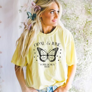 Pu&ograve; includere: Una maglietta gialla con una grafica di farfalla nera e il testo "OPAL & JUNE" e "YOUR DESIGN HERE".