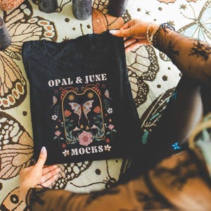 May include: Black t-shirt with a floral design and the text "OPAL & JUNE MOCKS" printed on the front.