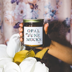 May include: A brown glass candle jar with a white label that says "OPAL and JUNE MOCKS". The label has a floral design and butterflies.
