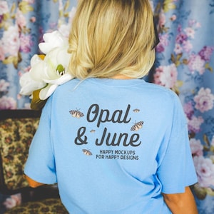 Könnte beinhalten: Ein hellblaues T-Shirt mit dem Text "Opal & June" in schwarzer Schrift. Der Text ist von kleinen schwarzen und weißen Schmetterlingsgrafiken umgeben. Der Text "Happy Mockups for Happy Designs" ist in Schwarz unter dem Haupttext gedruckt.