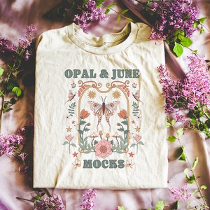 May include: A beige t-shirt with a graphic design featuring a butterfly, flowers, and the text "OPAL & JUNE MOCKS".