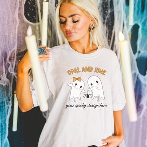 May include: White t-shirt with a graphic of two ghosts holding hands with a spider between them. The text "OPAL AND JUNE" is above the ghosts and "your spooky design here" is below.
