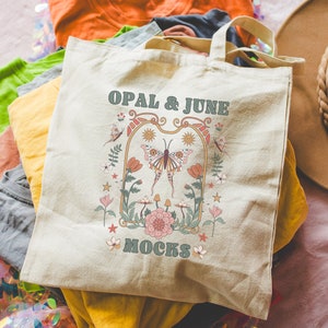May include: A beige canvas tote bag with a floral design and the text "OPAL & JUNE MOCKS". The bag is surrounded by colorful fabric scraps.